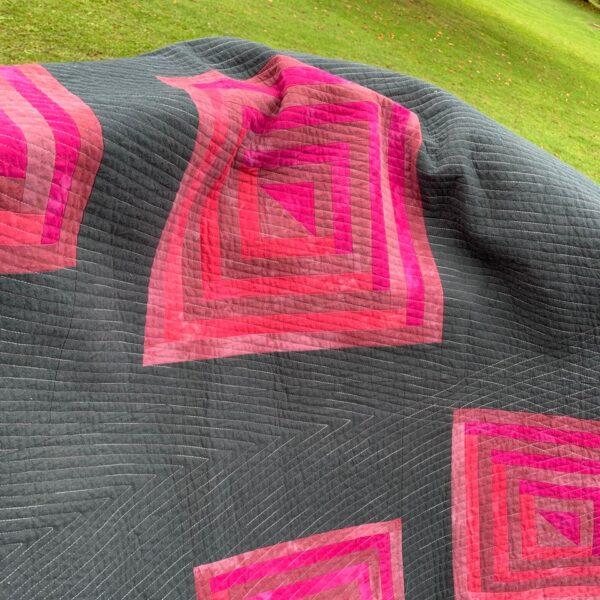 dark grey quilt with browns/pinks/reds log cabin blocks. Straight line quilting in variegated grey thread.