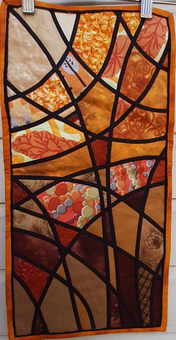 Stained glass applique quilt. Narrow black bias strips criss-crossing a gold multi background.