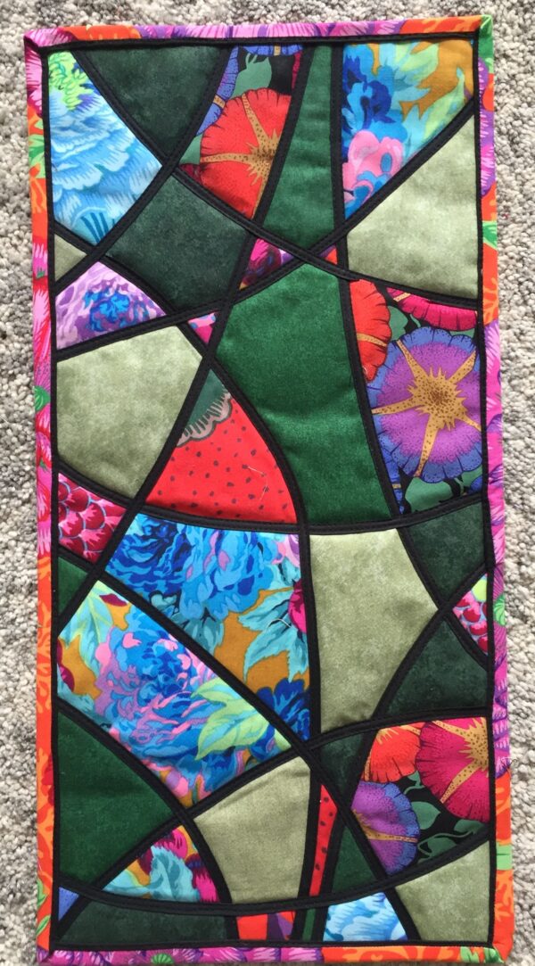 Stained glass applique quilt. Narrow black bias strips criss-crossing a blue and green multi background.