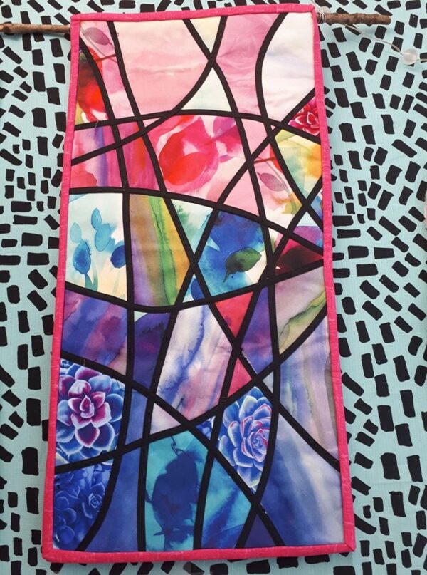 Stained glass applique quilt. Narrow black bias strips criss-crossing a pink and blue multi background.
