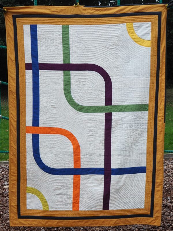 Going Underground quilt. Different coloured interlocking strips to represent underground lines on a cream background with mustard and black borders