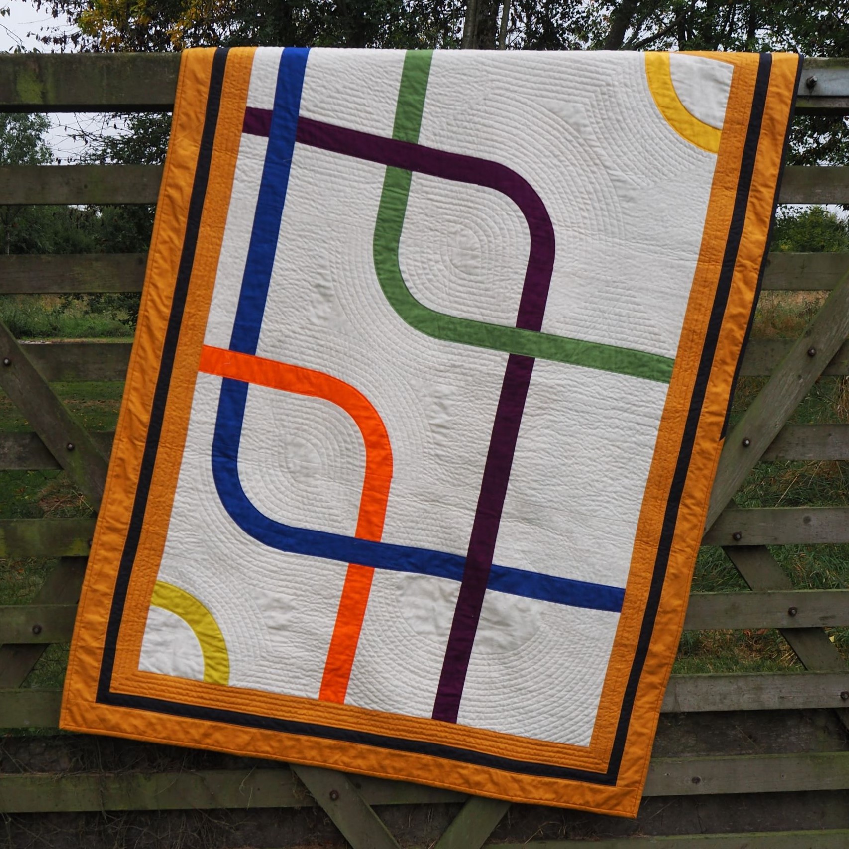Quilt made using Modern Adapted Drunkard's Path blocks in colours to reflect lines of the London Underground, set into a white background. Walking foot quilting