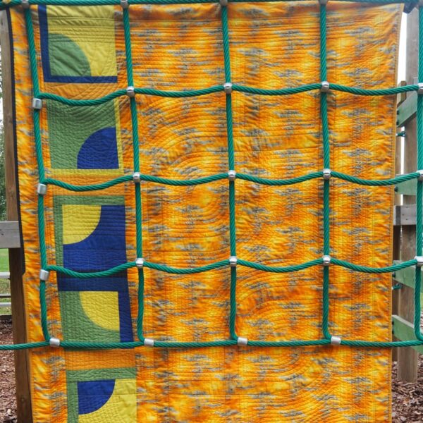 back of quilt showing through child's climbing ropes. Gold multi fabric with inserts of individual curved blocks