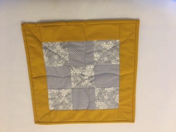 Absolute Beginner Sample - 9-patch block in grey floral and spotty fabrics with mustard border and binding. Wiggly starburst quilting