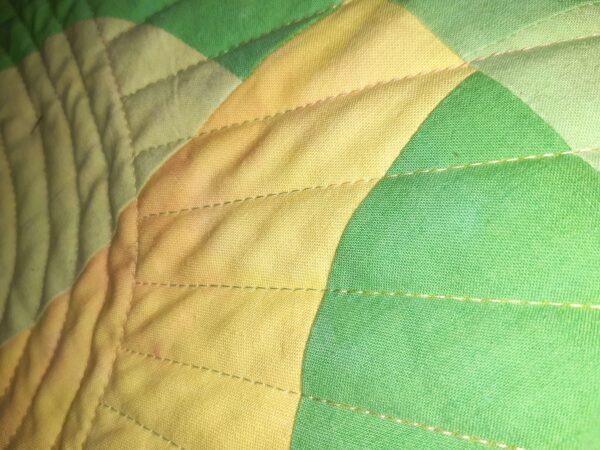 close up of green and yellow quilt highlighting curved piecing and walking foot quilting