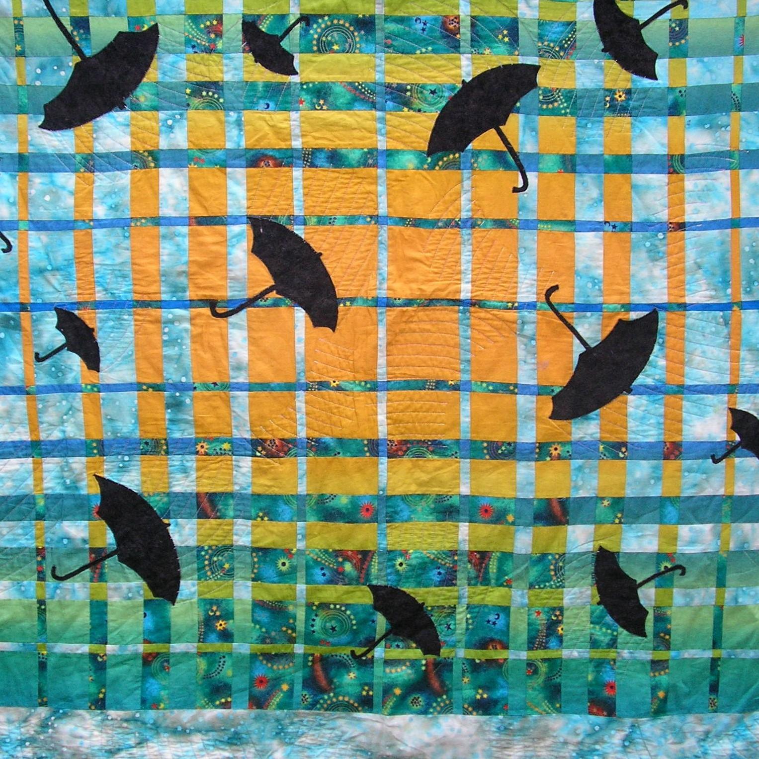 quilt in green, blue and orange squares and rectangles with black umbrella applique in difference sizes.